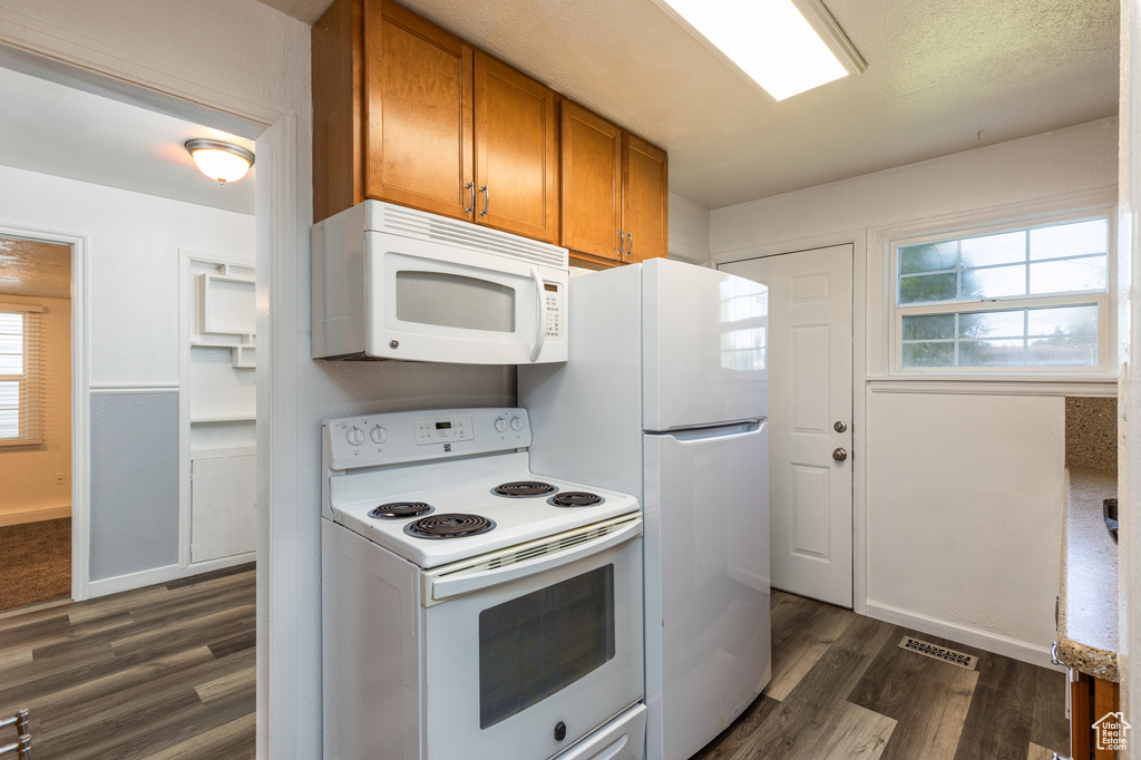 Kitchen with white appliances, brown cabinetry, dark wood-style flooring, baseboards, and healthy amount of natural light