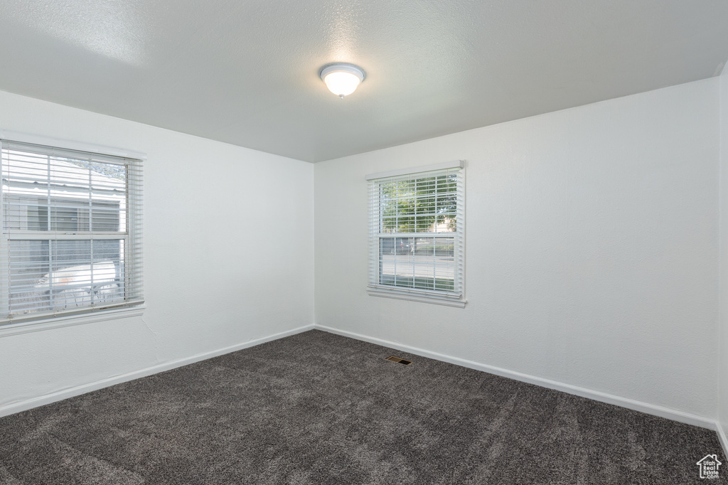 Spare room featuring dark carpet and baseboards