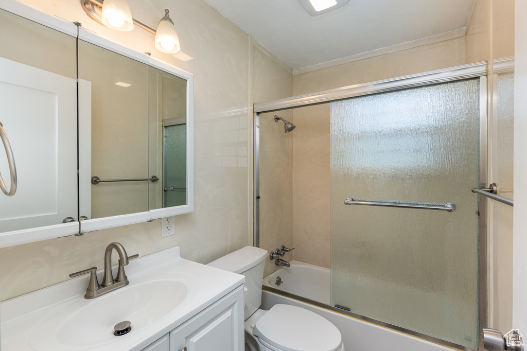 Bathroom with toilet, vanity, and shower / bath combination with glass door