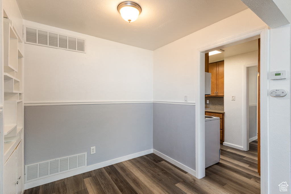 Empty room with dark wood-type flooring, washer / clothes dryer, and baseboards