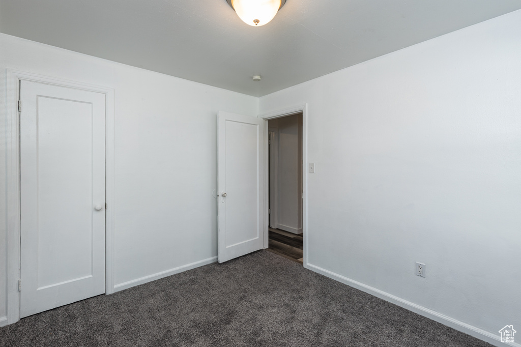 Unfurnished bedroom with dark colored carpet and baseboards