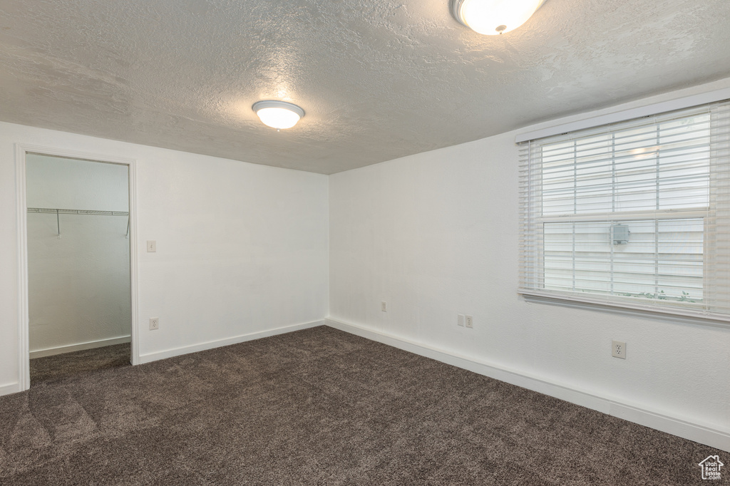 Unfurnished bedroom with dark carpet, a textured ceiling, baseboards, and a closet