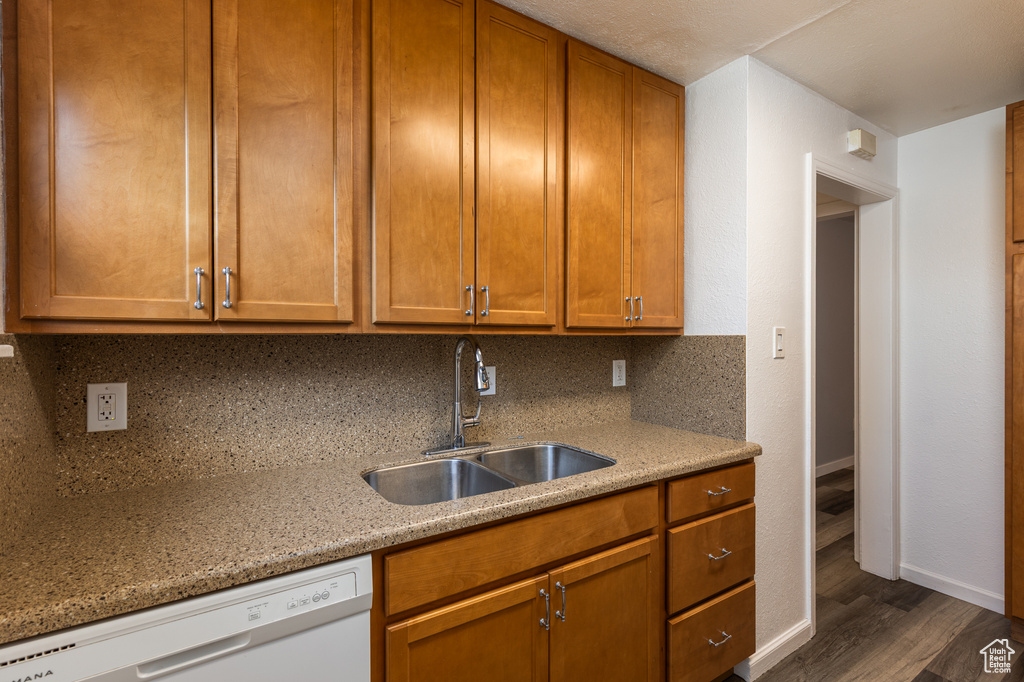 Kitchen with white dishwasher, a sink, baseboards, dark wood-type flooring, and backsplash