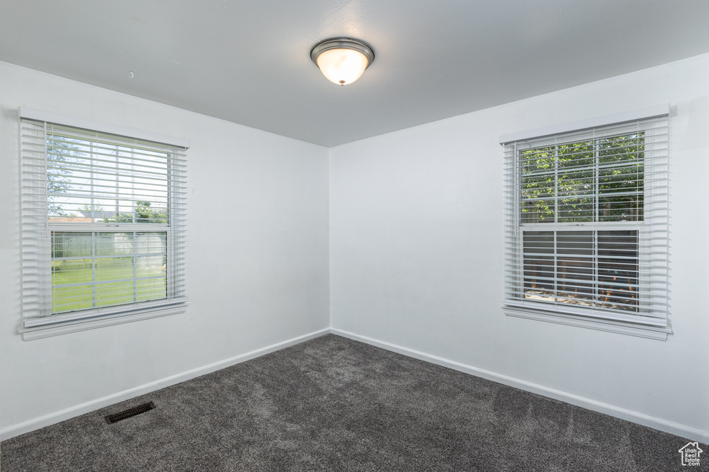 Unfurnished room with dark carpet, healthy amount of natural light, and baseboards