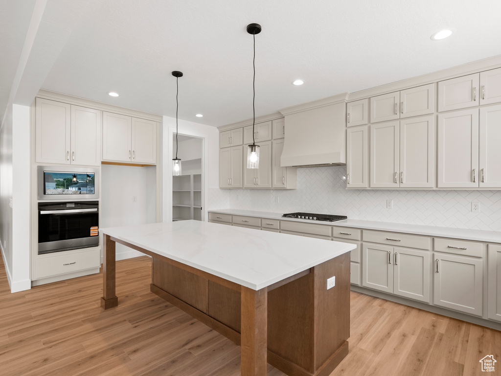 Kitchen featuring black appliances, premium range hood, light wood-style floors, tasteful backsplash, and recessed lighting