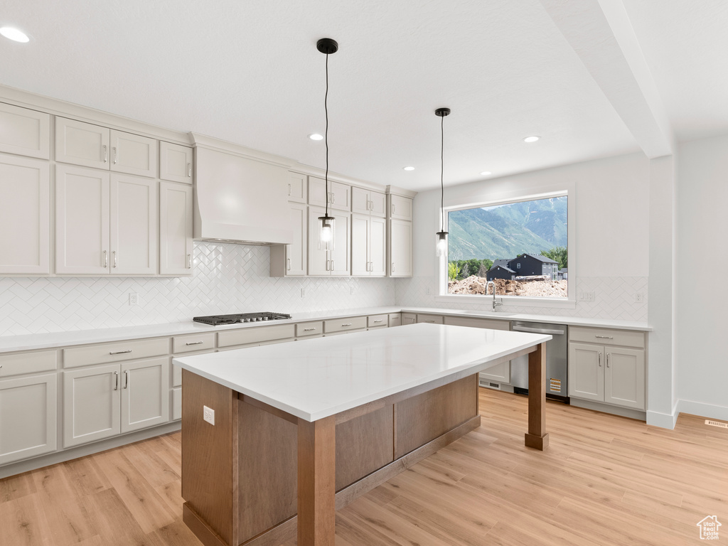 Kitchen with stainless steel dishwasher, light wood-type flooring, custom exhaust hood, decorative backsplash, and light countertops