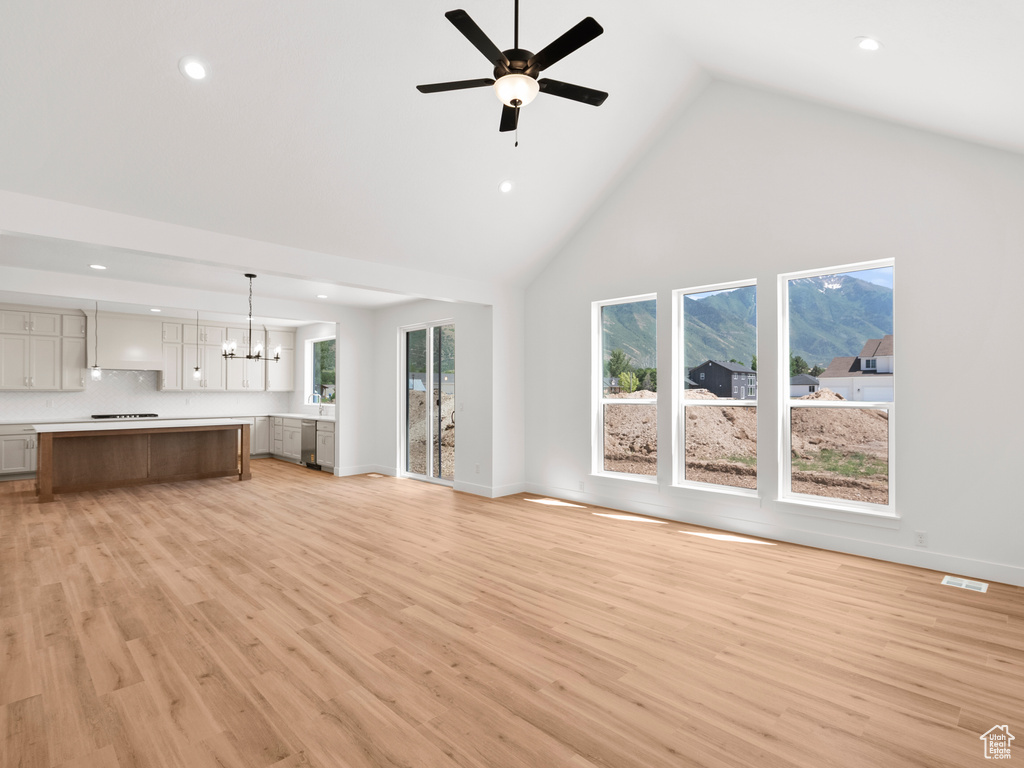 Unfurnished living room with high vaulted ceiling, recessed lighting, ceiling fan, light wood-style flooring, and a chandelier