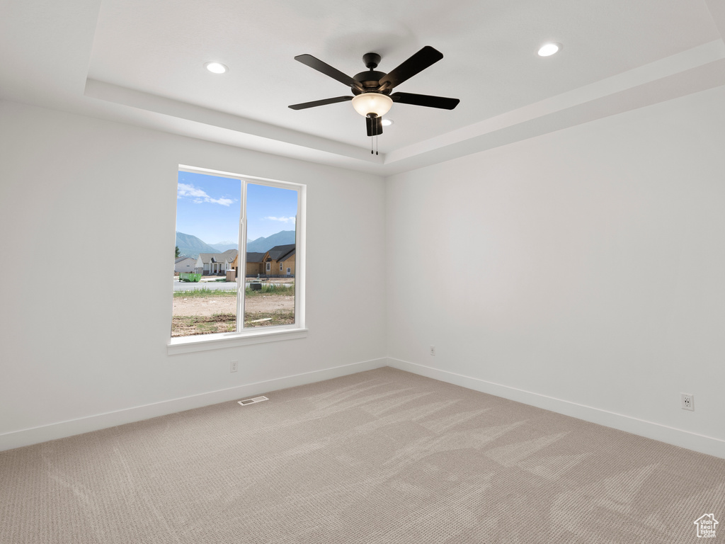 Empty room featuring a tray ceiling, light colored carpet, recessed lighting, and ceiling fan