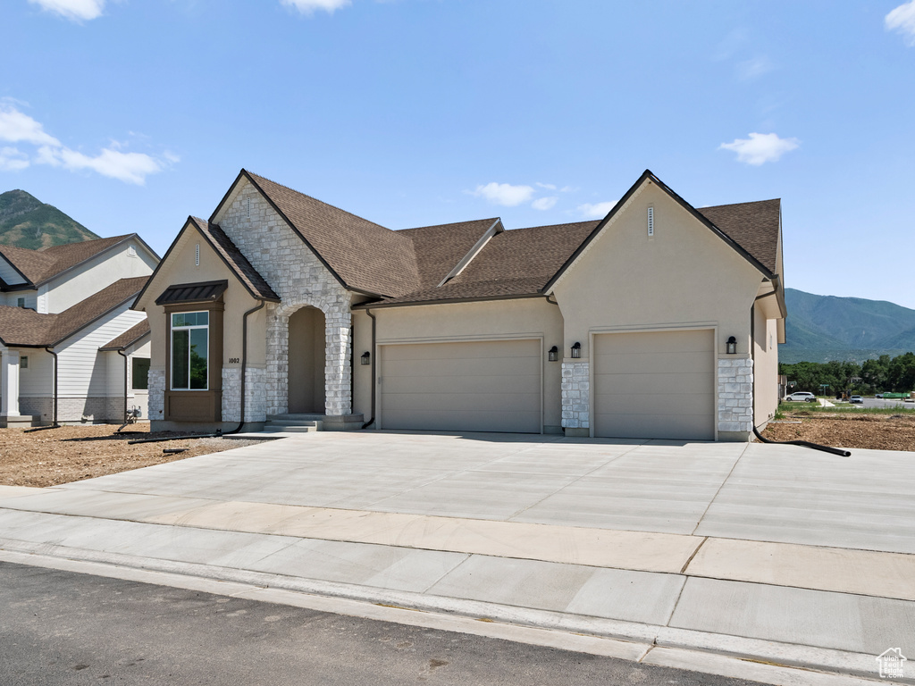 French provincial home with stone siding, an attached garage, driveway, a mountain view, and stucco siding