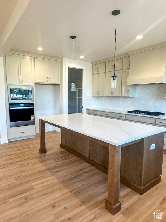 Kitchen with oven, gas stovetop, custom range hood, backsplash, and light wood-type flooring