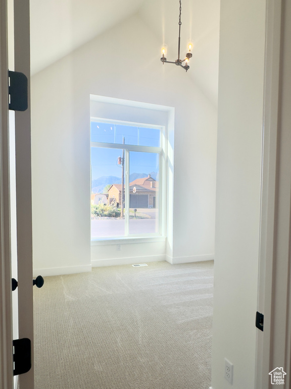 Carpeted empty room featuring lofted ceiling, a chandelier, and baseboards