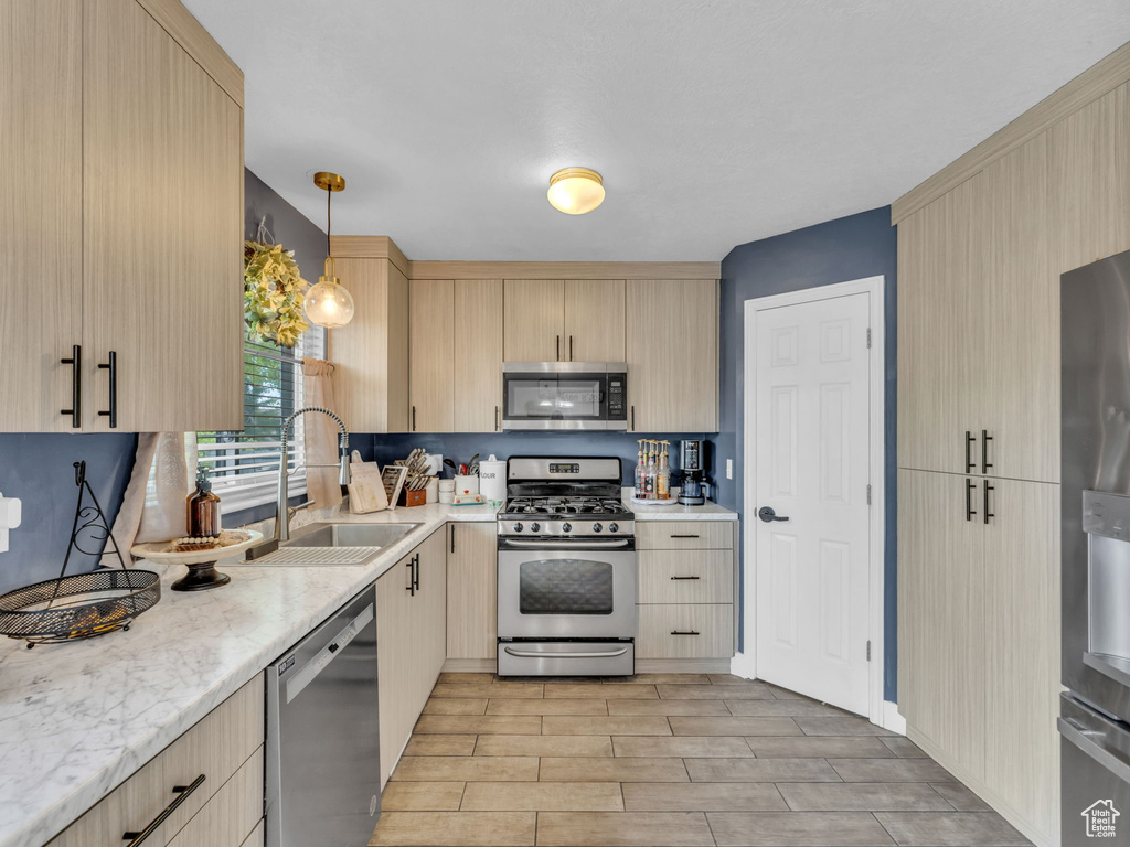 Kitchen featuring appliances with stainless steel finishes, light brown cabinetry, a sink, light wood-style floors, and pendant lighting