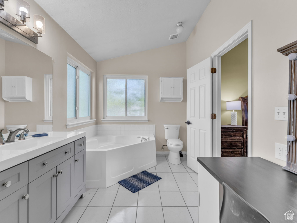Full bath with vanity, lofted ceiling, a garden tub, toilet, and tile patterned flooring