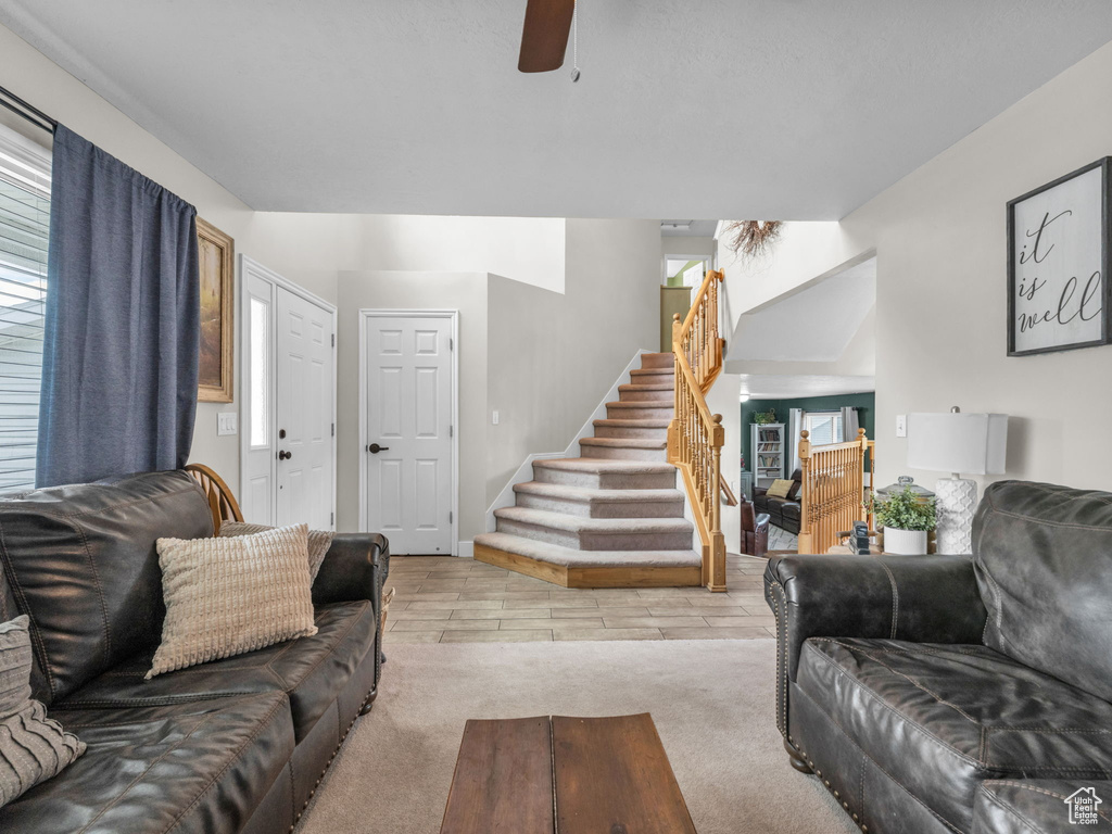 Living area featuring stairs, a ceiling fan, carpet floors, and plenty of natural light