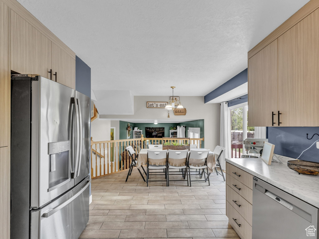 Kitchen with appliances with stainless steel finishes, light brown cabinetry, decorative light fixtures, and light wood finished floors