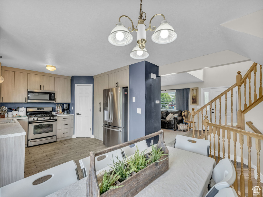 Kitchen featuring stainless steel appliances, light brown cabinetry, light countertops, a sink, and open floor plan