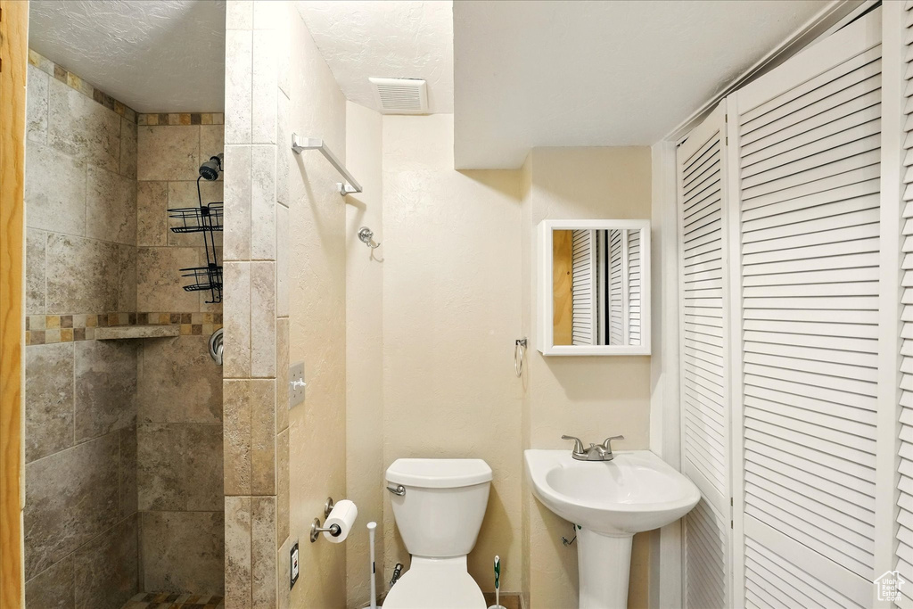 Bathroom with a tile shower, toilet, a sink, and a closet