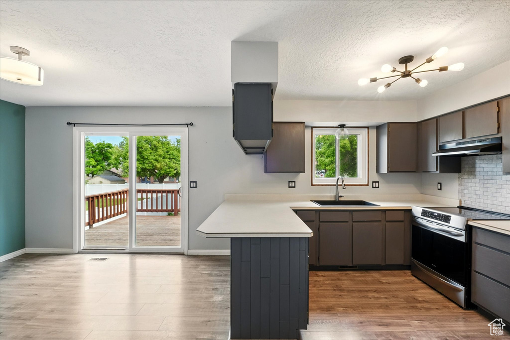 Kitchen with electric range, a sink, under cabinet range hood, a peninsula, and a textured ceiling