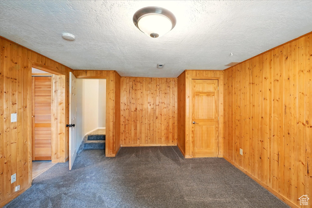 Spare room with wooden walls, dark colored carpet, a textured ceiling, a smoke detector, and baseboards