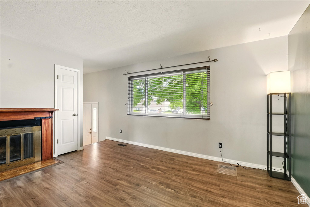 Unfurnished living room featuring a glass covered fireplace, baseboards, wood finished floors, and a textured ceiling