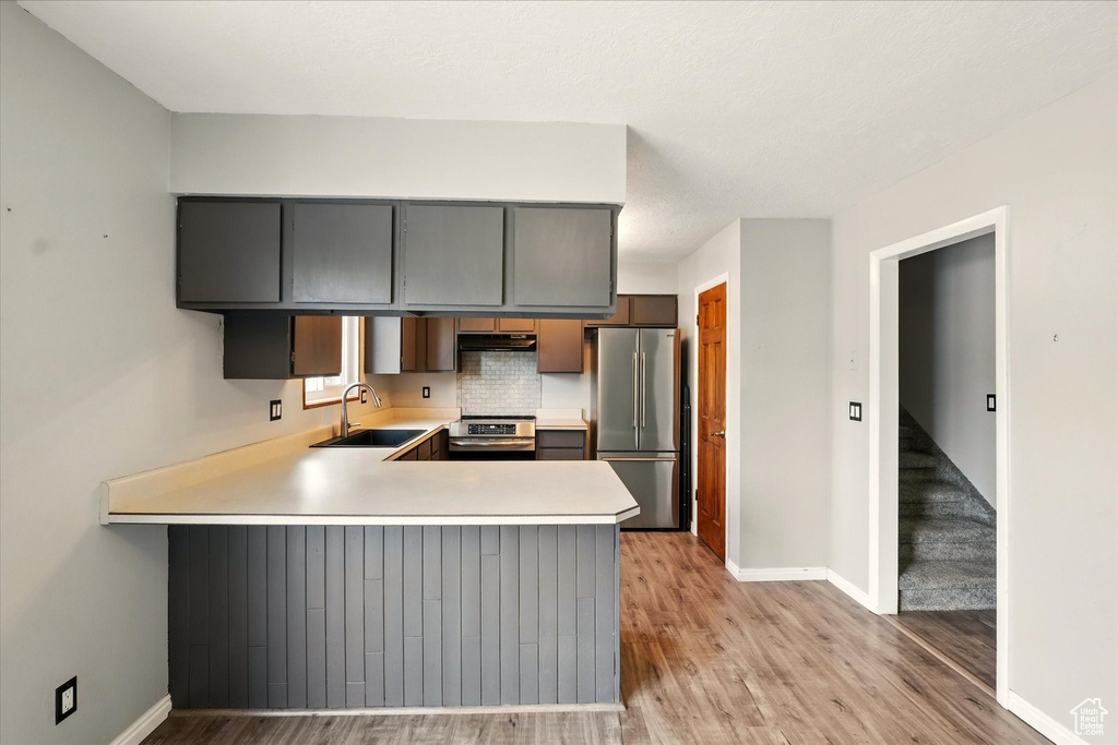 Kitchen with stainless steel appliances, a sink, baseboards, light countertops, and a peninsula