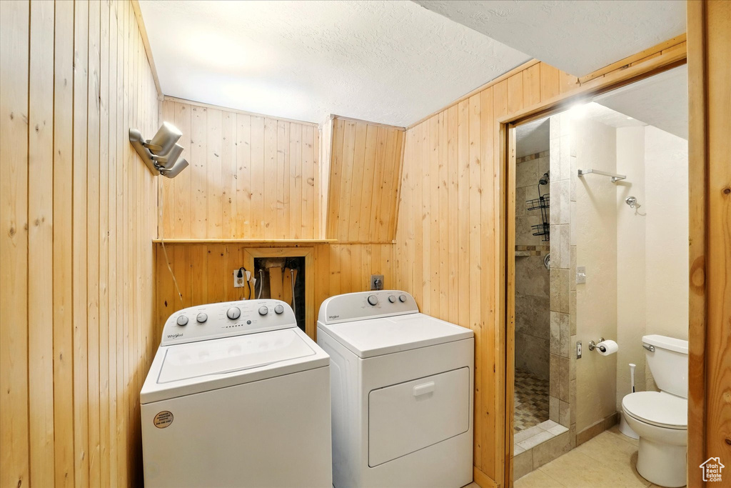 Laundry room with wooden walls, washing machine and dryer, and light tile patterned floors