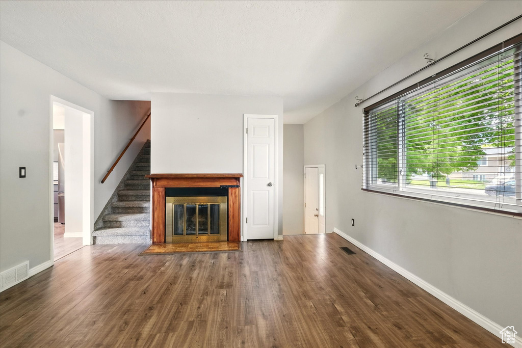 Unfurnished living room with wood finished floors, baseboards, stairs, and a glass covered fireplace