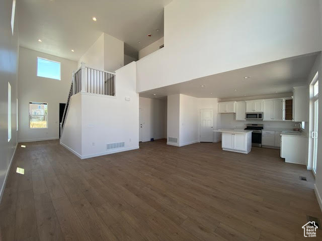 Unfurnished living room featuring a high ceiling, wood finished floors, and recessed lighting