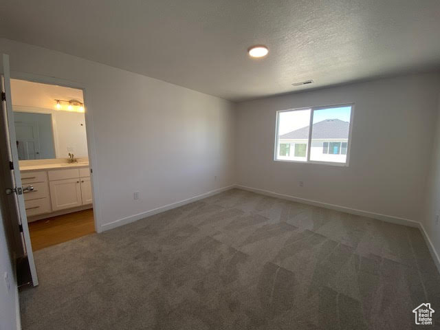 Unfurnished bedroom featuring light colored carpet, ensuite bath, and a textured ceiling