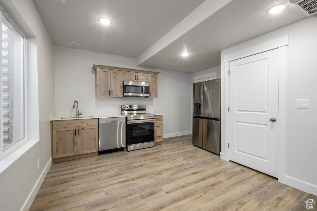 Kitchen with stainless steel appliances, a sink, light brown cabinetry, baseboards, and light wood-type flooring
