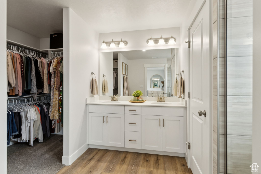 Full bath featuring double vanity, wood finished floors, a walk in closet, and baseboards