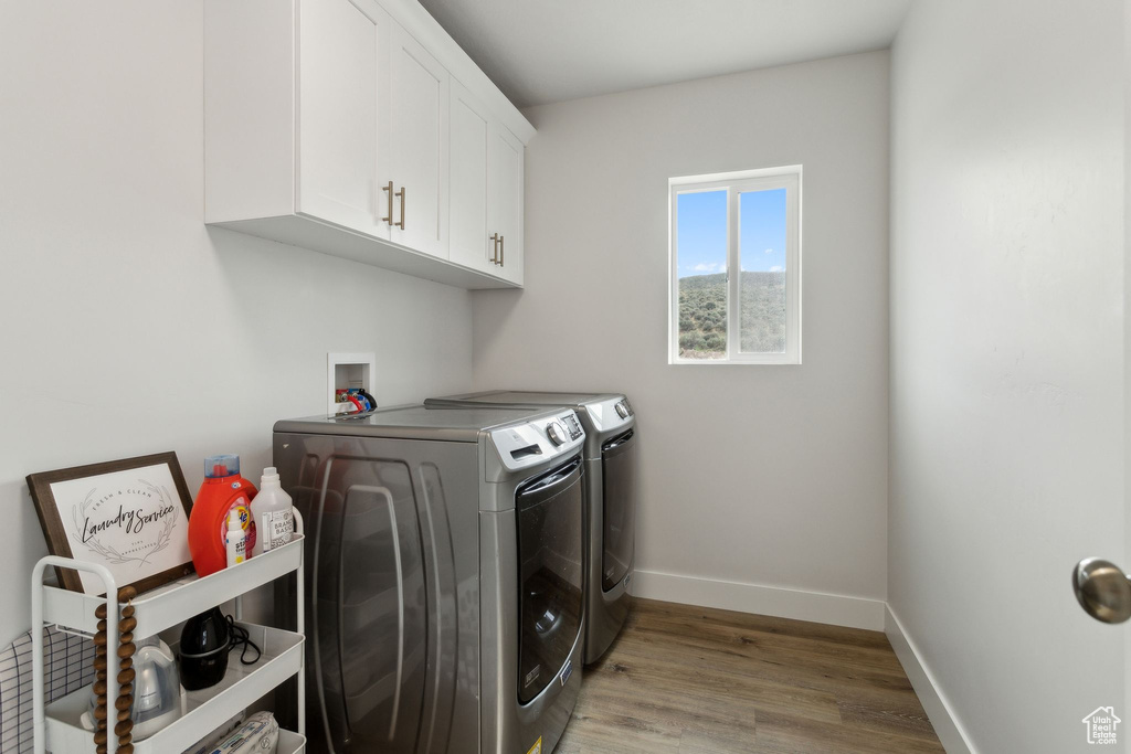 Clothes washing area with washing machine and clothes dryer, cabinet space, light wood finished floors, and baseboards