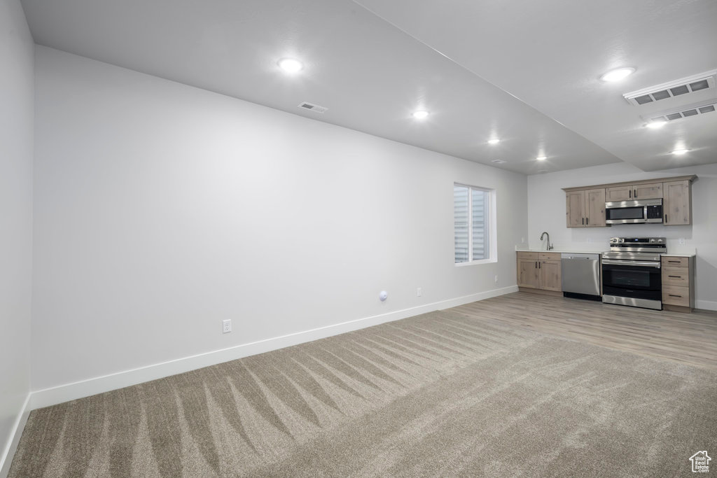 Unfurnished living room with light colored carpet, baseboards, recessed lighting, and a sink