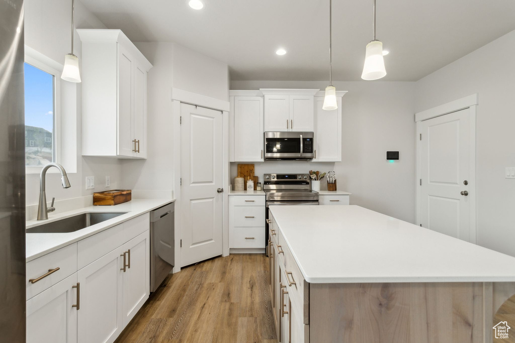 Kitchen with stainless steel appliances, a sink, light wood finished floors, a center island, and light countertops
