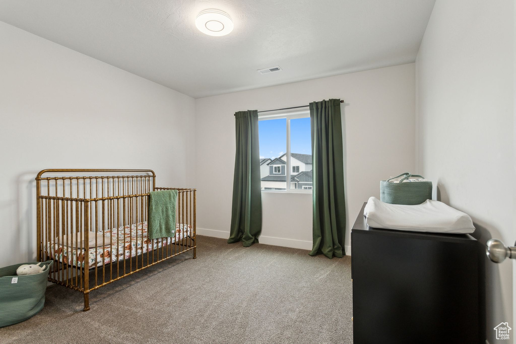 Carpeted bedroom featuring a crib and baseboards