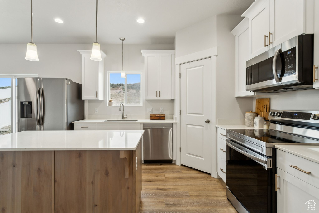 Kitchen featuring stainless steel appliances, a sink, white cabinets, light wood-style flooring, and light countertops