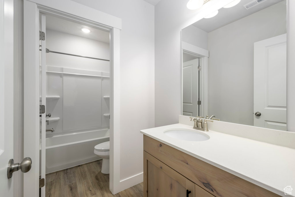 Bathroom featuring wood finished floors, toilet, vanity, and bathtub / shower combination