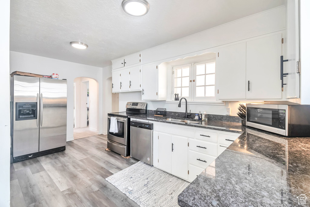 Kitchen with stainless steel appliances, a sink, white cabinets, dark stone counters, and arched walkways