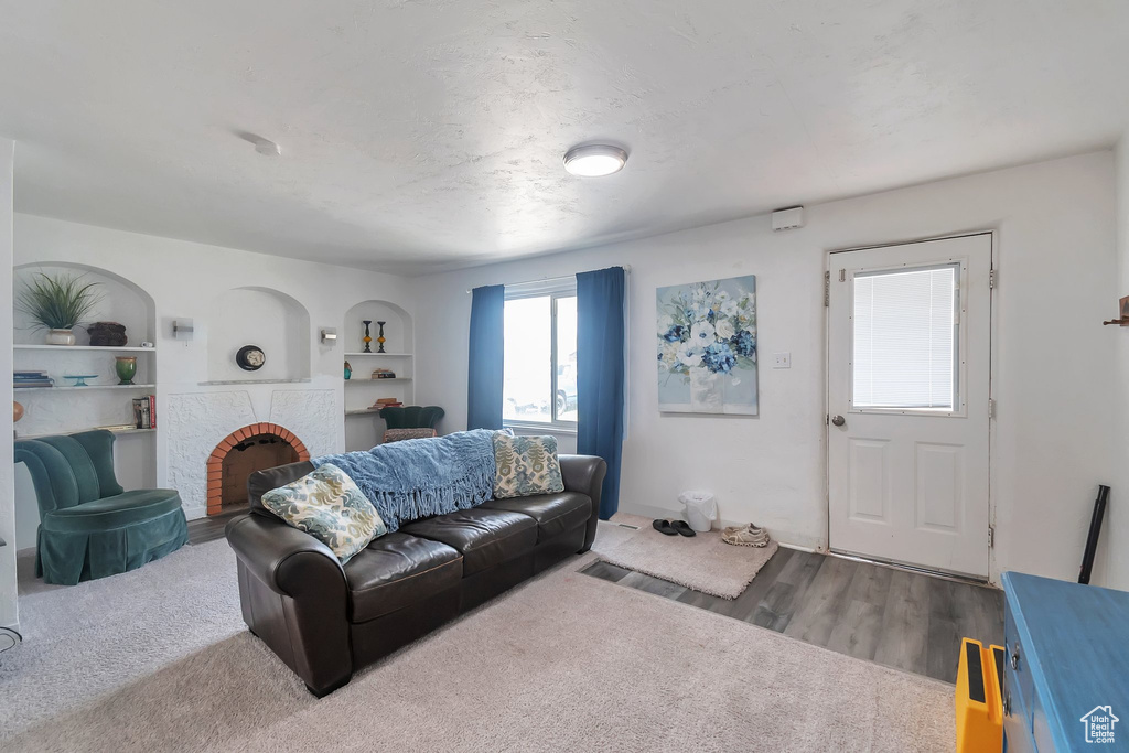 Living area with a brick fireplace, wood finished floors, and built in shelves