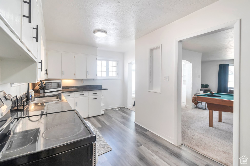 Kitchen with black range with electric stovetop, stainless steel microwave, white cabinetry, a textured ceiling, and billiards