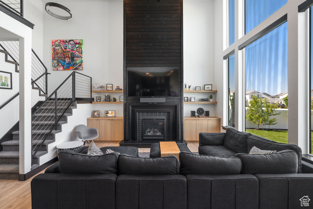Living area featuring wood finished floors, a towering ceiling, stairs, and a glass covered fireplace