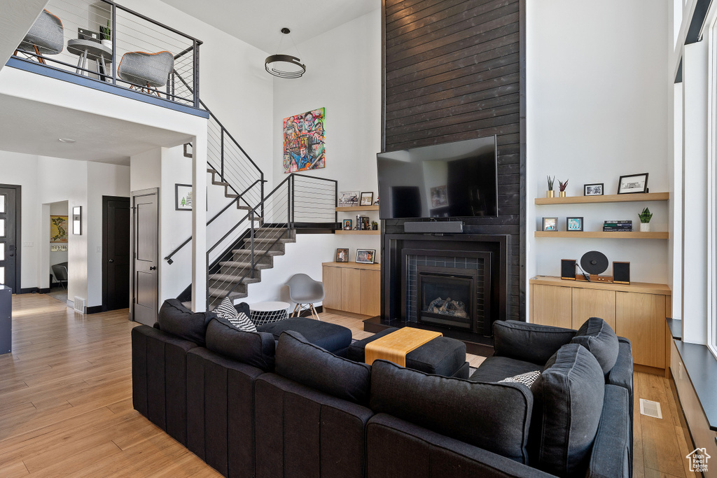 Living room with a towering ceiling, light wood-style floors, a fireplace, and stairs