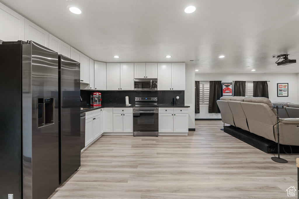 Kitchen featuring stainless steel appliances, open floor plan, dark countertops, white cabinetry, and light wood-type flooring
