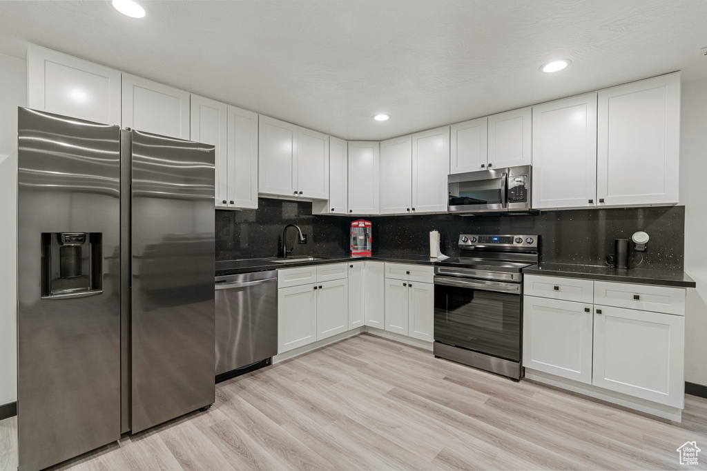 Kitchen featuring stainless steel appliances, dark countertops, white cabinets, backsplash, and recessed lighting