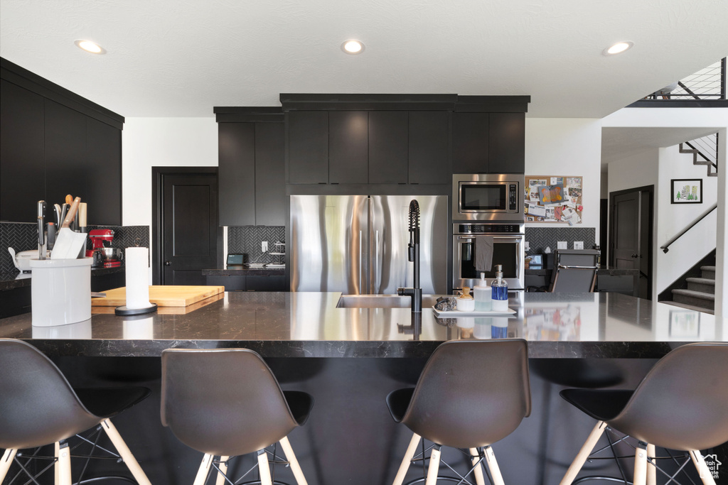 Kitchen featuring appliances with stainless steel finishes, dark cabinetry, a kitchen breakfast bar, tasteful backsplash, and recessed lighting