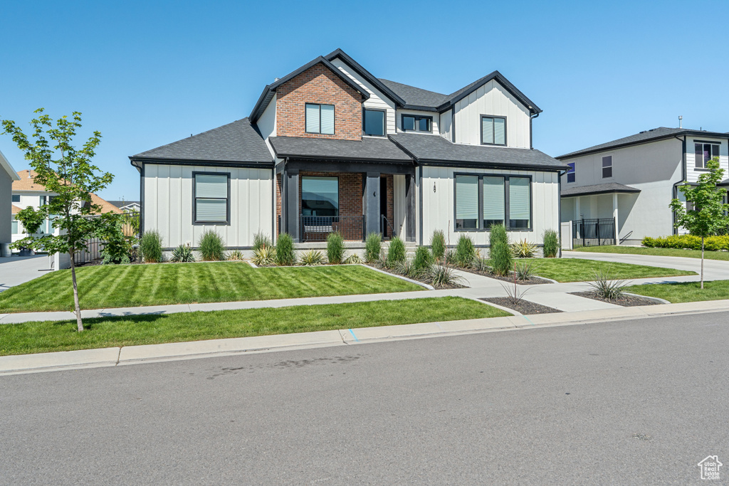 Modern farmhouse style home with board and batten siding, a front yard, and a shingled roof