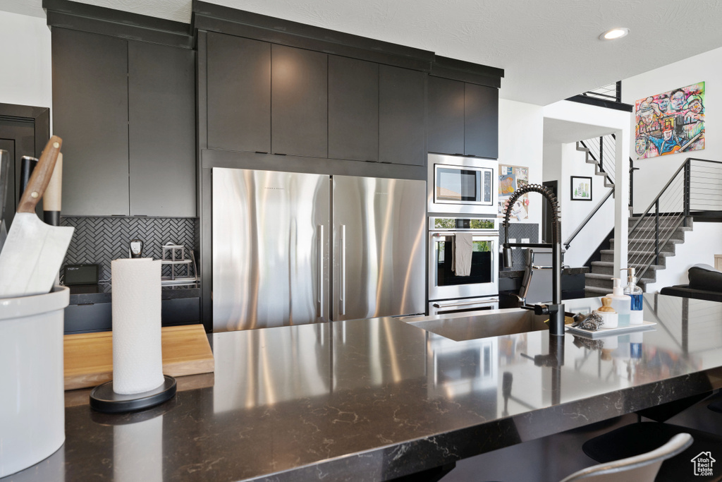 Kitchen featuring appliances with stainless steel finishes, backsplash, a sink, dark stone countertops, and recessed lighting