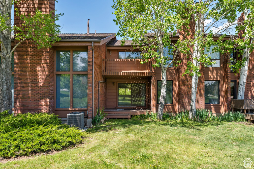 Back of house with cooling unit, a lawn, a chimney, and a balcony