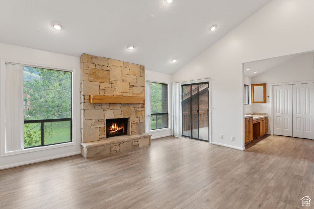 Unfurnished living room featuring vaulted ceiling, a fireplace, light wood-style flooring, recessed lighting, and baseboards