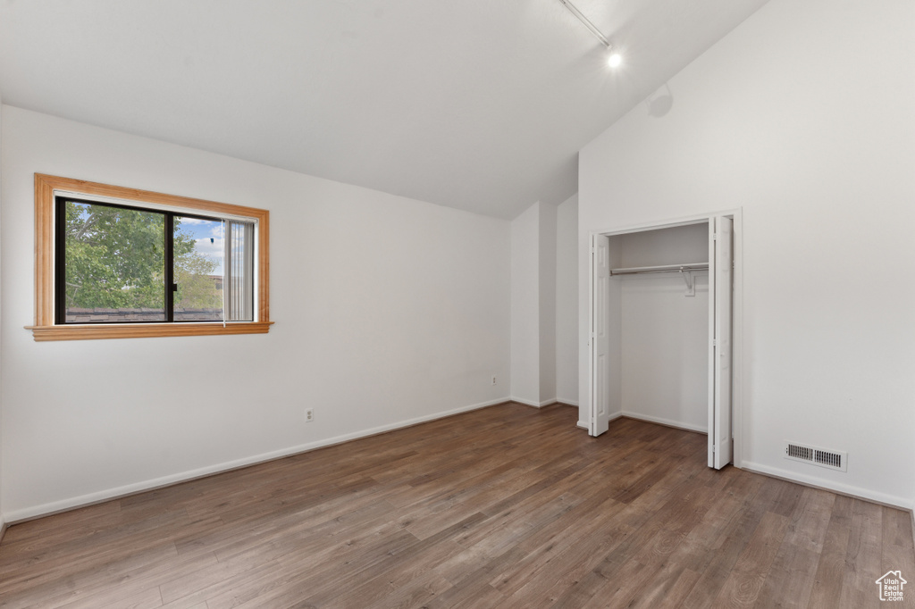 Unfurnished bedroom featuring wood finished floors, lofted ceiling, baseboards, and track lighting